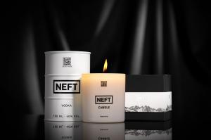 A lit NEFT candle sits between a white barrel of NEFT Vodka and the candle box on a glass table with a black fabric backdrop