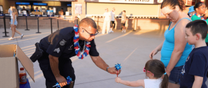 A police officer hands a small sparkler to a young girl, while her family watches, at an outdoor event.