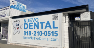 Front view of the Nuevo Dental sign in North Hollywood, CA, advertising dental services with a smiling tooth mascot, contact phone number, website, and a QR code.