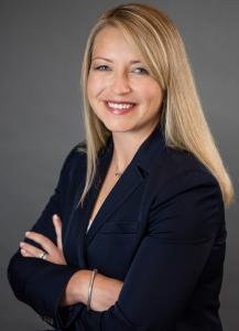 Image of a Caucasian blond woman smiling with her arms crossed and wearing a dark blue blazer