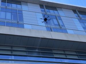 A drone performing exterior cleaning on the glass windows of Lundquist Tower at Torrance Memorial Medical Center (TMMC), demonstrating SprayTech’s advanced drone-powered maintenance technology.