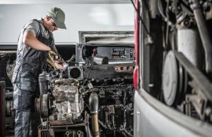 Diesel technician repairing a truck engine inside a truck repair shop, using professional tools for maintenance and diagnostics.