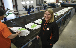 Lana Corsano in front of printed t-shirts on conveyer to dryer.