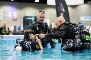 Two Scuba instructors in pool with attendee at the Scuba Show demonstrating how to dive