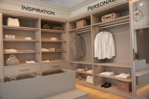 A luxurious custom closet display in PLC Closets' showroom, featuring sleek shelving, built-in storage, soft lighting, and elegant clothing and accessories arranged under 'Inspiration' and 'Personalization' signage.
