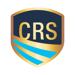 This image shows the CRS (Certified Residential Specialist) logo in the form of a shield-shaped emblem. The shield has a gold/bronze border with a navy blue upper section containing the letters "CRS" in gold. The lower portion of the shield features two c