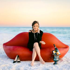 Linda Miller sits gracefully on a giant red lip-shaped sofa on the pristine white sands of Scenic Highway 30A.