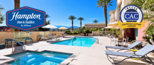 Outdoor pool area at Hampton Inn & Suites, featuring lounge chairs, umbrellas, and palm trees against a clear blue sky.