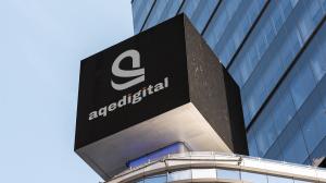 AQe Digital logo displayed on a cube-shaped billboard against a vibrant cityscape