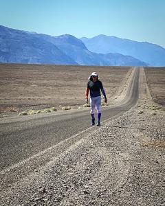 Frank McKinney walks on a long, empty road. There are distant mountains in the background under a clear sky.