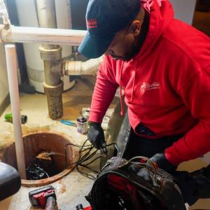 J. Blanton Plumbing technician fixing a sump pump, highlighting the company’s expertise in sump pump maintenance, basement flooding prevention, and 24-hour plumbing services for spring readiness.