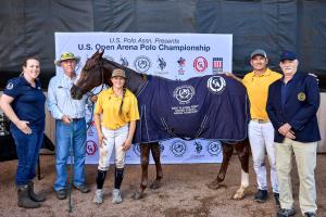 an arena polo pony proudly wears her winning blanket for Best Playing Pony.  She is surrounded by her player, trainer, owner and admirerers