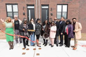 A diverse group of people celebrating after cutting a ribbon standing outside on a Philly street in front of new construction rowhomes