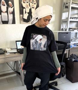 sister camilla, standing in the shipping room, with images on the wall behind her of other sisters, and Camilla is looking down at the t-shirt she is wearing and promoting