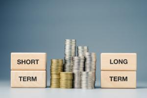 Stack of coins next to wooden blocks reading 'short term' and 'long term'