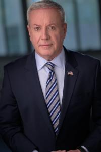 Actor and writer Mark Pettit in a dark suit, blue shirt and striped tie.