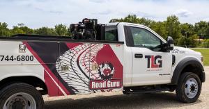Picture of a mobile service repair truck for semi-trucks. It is white with red and black striping and designs. It also has TLG and Road Guru logos.