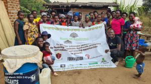 Group of women and children in Kyangwali Refugee Settlement holding a Roots of Resilience banner during a mushroom farming training session.