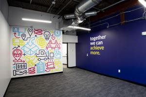 Interior of Elevator co-warehousing space showing a colorful wall mural with business icons and symbols alongside a navy blue wall with the text "together we can achieve more."