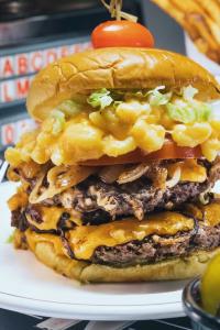 Close-up of Diner 24 NYC's 12oz Smash Burger with melted cheese, lettuce, tomato, grilled onions, and mac and cheese on a toasted bun.