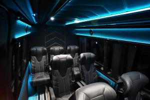 Interior of Mercedes-Benz Sprinter VIP minibus featuring premium black leather seats with diamond stitching, blue ambient lighting throughout the cabin, and luxury executive transportation design