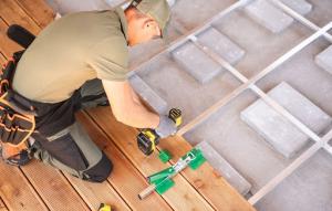  A worker focused on deck installation using power tools to secure patio flooring on a wooden deck.