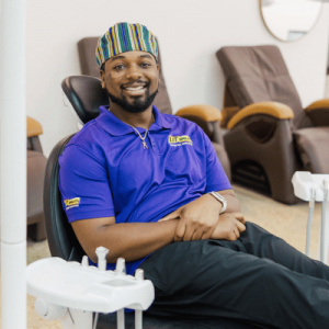 A person in a blue polo shirt sits in a dental chair, surrounded by comfortable seating in a modern dental office.