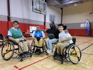 Four adaptive athletes in wheelchairs pose for a photo on a basketball court