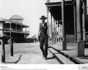  A man dressed in a cowboy hat and vest walks down an abandoned Western Main Street.