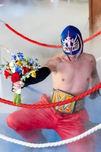 Man dressed as a luchador with WWE Champion belt holds a wedding bouquet inside a ring at Viva Las Vegas Wedding Chapel