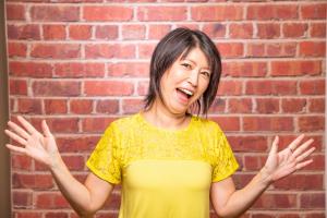 Middle age Japanese American mom standup comedian, Michelle MaliZaki in her signature yellow dress