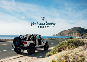 Open-top Jeep parked along Pacific Coast Highway in Ventura County, California, with people enjoying ocean views, mountains in the background, and the new Ventura County Coast logo featured prominently.