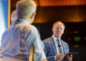 Dr. Greg Mattingly serves on a panel at a conference, pictured with two other men blurred in the foreground.