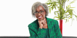 Jennifer L. Smith smiling confidently while seated, wearing a green floral-patterned blazer, with a potted plant in the background.