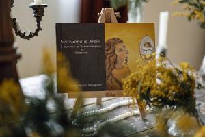 My Name Is Areni: A Journey of Remembrance & Renewal on an easel surrounded by flowers.