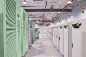 Interior of Sinexcel-RE’s battery test equipment factory, featuring organized rows of green and white testing units with status indicator lights, in a clean, well-lit facility with overhead cooling and electrical systems.