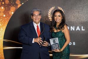 man and women smiling  with award for jose pereira at international impact book awards with black background