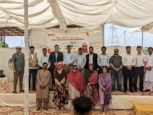 A group of people are gathered for a photo in front of a sign that reads Eco-Friendly Bricks are now available in Sindh province.