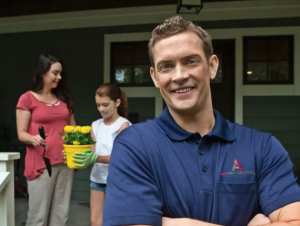 A pest control exterminator from A-1 Pest Control poses. A mom and daughter hold a pot of yellow flowers in the background.