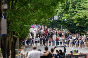 A crowd of people watch the Kennett Memorial Day Parade on a tree lined street in Kennett Square.