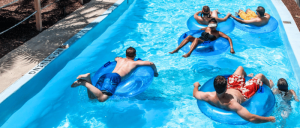 A bustling wave pool filled with families and children, enjoying inflatable tubes under a sunny sky at a water park.