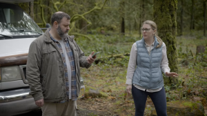 A man and woman standing in front of an RV. The man is looking down at his phone and the woman is looking at him.