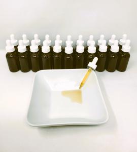 a row of 2 oz amber bottles with droppers and a bowl in front with one dropper spilling oil into the bowl