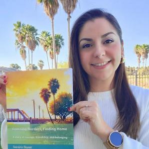Sarairis Slusser smiling and holding her award-winning children's book, Crossing Borders, Finding Home.