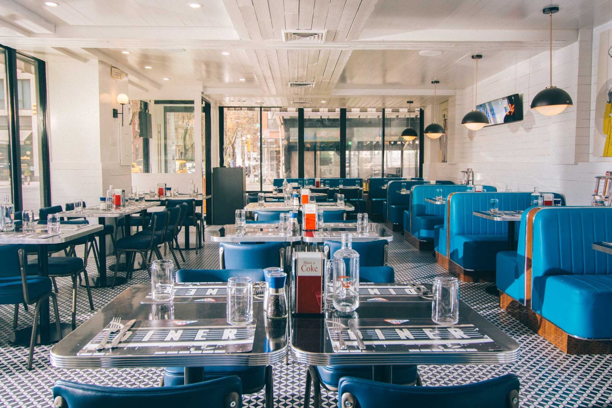 Interior of Diner 24 NYC featuring blue booths, black-and-white tiled floors, and a bright, retro-inspired atmosphere.