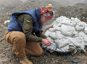 Ukrainian female deminer in personal protective equipment performing an explosive ordnance disposal demolition exercise as part of the certification testing to complete her International Mine Action Standards practical examinations