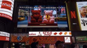 Two floral rose bears in red and pink, featuring a yellow heart and the letter “U”, displayed in an acrylic case with New York taxis in the background.