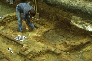 We see an individual excavating a medieval brothel. The ovens are revealed, which were used to heat wooden bathtubs positioned above these features.