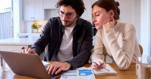 a man and woman review their electricity bill while looking at electricity plan options online.