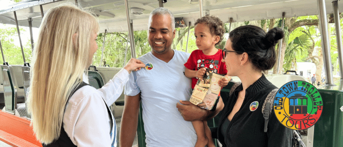 A woman in a black vest hands a pamphlet to a man in a light shirt, while a child sits in his arms, smiling.